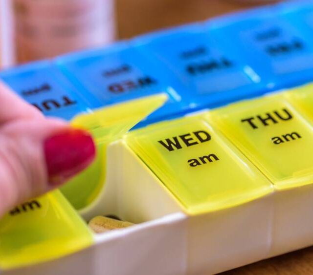 Hand placing medication into a weekly pill organizer