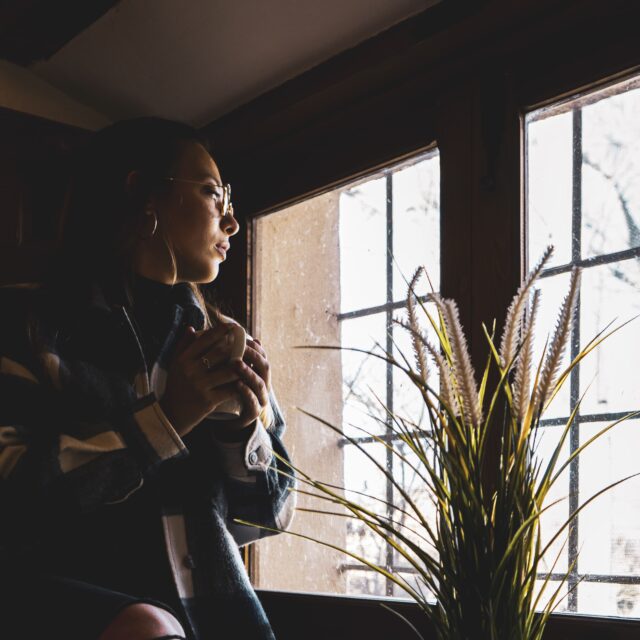 Young woman sitting calmly by a window with a warm drink