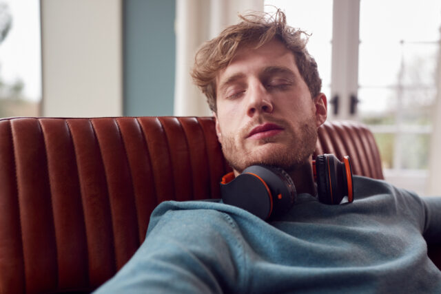 Man resting on a couch with eyes closed and headphones around his neck