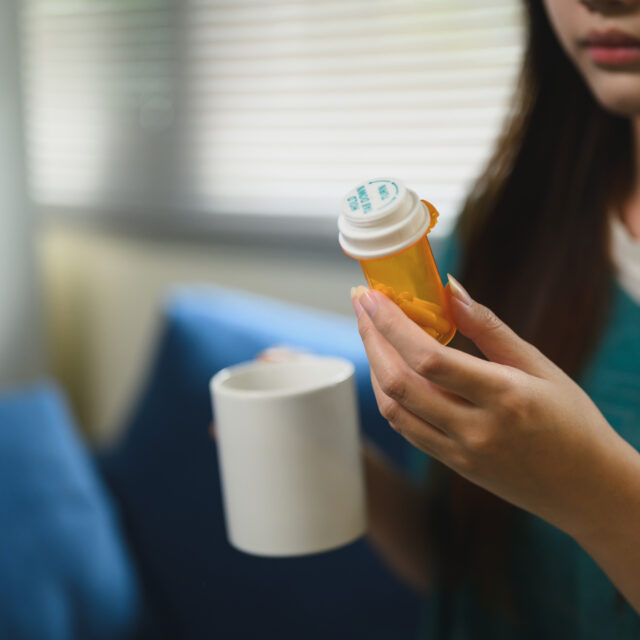 Woman holding a prescription medication bottle and a mug at home
